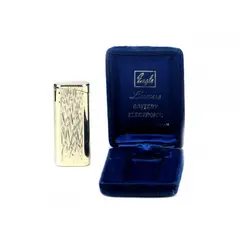 Foto de um(a) Antigo isqueiro EAGLE/ LUXUS, da categoria de Isqueiros e isqueiros. Antigo isqueiro em metal dourado da manufatura EAGLE/ LUXUS BATTERY ELECTRONIC JAPAN.No estojo original em veludo azul.... Vendido no marketplace Trésors.