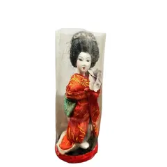 Foto de um(a) Pequena Gueixa Japonesa, Década de 1960, da categoria de Modelos e estatuetas. Pequena gueixa com seu quimono original dos anos 1960. Ainda com a embalagem. A: 12 cm / Diâmetro: 4,6 cm / Peso: 38 g. Vendido no marketplace Trésors.