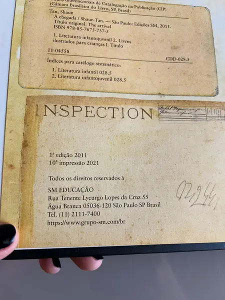 Foto de um(a) Livro de ilustrações decorativo em capa dura, da categoria de Livros. Livro capa dura, de 2021, em português, mas ele é somente com ilustrações. Conta história de imigrantes. Leves marcas do... Mostrado de uma perspectiva diferente. Vendido no marketplace Trésors.