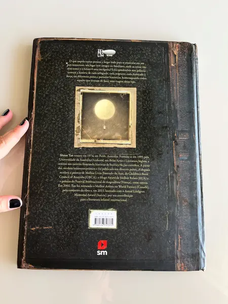 Foto de um(a) Livro de ilustrações decorativo em capa dura, da categoria de Livros. Livro capa dura, de 2021, em português, mas ele é somente com ilustrações. Conta história de imigrantes. Leves marcas do... Mostrado de uma perspectiva diferente. Vendido no marketplace Trésors.