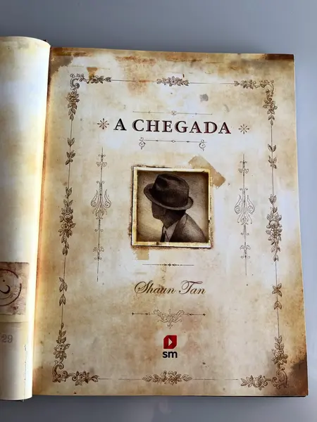 Foto de um(a) Livro de ilustrações decorativo em capa dura, da categoria de Livros. Livro capa dura, de 2021, em português, mas ele é somente com ilustrações. Conta história de imigrantes. Leves marcas do... Mostrado de uma perspectiva diferente. Vendido no marketplace Trésors.