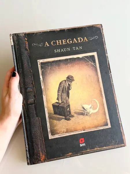 Foto de um(a) Livro de ilustrações decorativo em capa dura, da categoria de Livros. Livro capa dura, de 2021, em português, mas ele é somente com ilustrações. Conta história de imigrantes. Leves marcas do... Mostrado de uma perspectiva diferente. Vendido no marketplace Trésors.