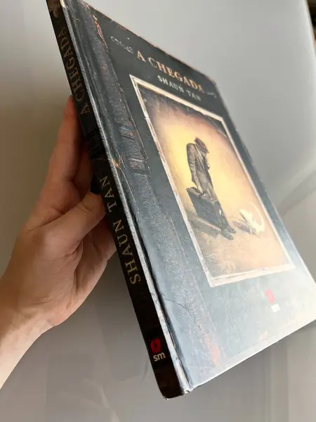 Foto de um(a) Livro de ilustrações decorativo em capa dura, da categoria de Livros. Livro capa dura, de 2021, em português, mas ele é somente com ilustrações. Conta história de imigrantes. Leves marcas do... Mostrado de uma perspectiva diferente. Vendido no marketplace Trésors.