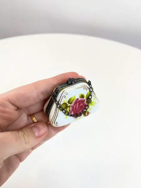 Foto de um(a) ​Porta pílulas em porcelana e metal - formato bolsinha, da categoria de Outros colecionáveis. Porta pílulas em porcelana e metal no formato de bolsinha. Mínimas marcas do tempo e uso. Medidas: 6x3cm. Mostrado de uma perspectiva diferente. Vendido no marketplace Trésors.
