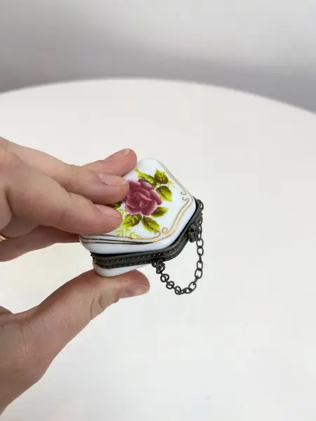 Foto de um(a) ​Porta pílulas em porcelana e metal - formato bolsinha, da categoria de Outros colecionáveis. Porta pílulas em porcelana e metal no formato de bolsinha. Mínimas marcas do tempo e uso. Medidas: 6x3cm. Mostrado de uma perspectiva diferente. Vendido no marketplace Trésors.