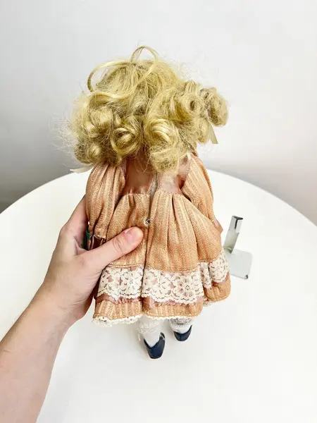 Foto de um(a) ​Boneca de porcelana, da categoria de Brinquedos e Hobbies. Boneca de porcelana com leves marcas do tempo e uso. Com suporte. Medidas: 30x16cm. Mostrado de uma perspectiva diferente. Vendido no marketplace Trésors.