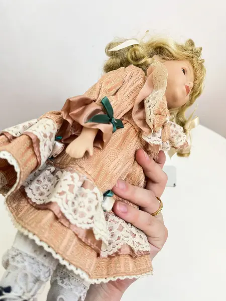 Foto de um(a) ​Boneca de porcelana, da categoria de Brinquedos e Hobbies. Boneca de porcelana com leves marcas do tempo e uso. Com suporte. Medidas: 30x16cm. Mostrado de uma perspectiva diferente. Vendido no marketplace Trésors.