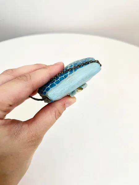 Foto de um(a) ​Bolsinha colecionável em resina, da categoria de Outros colecionáveis. Bolsinha colecionável em resina com alça em corrente metálica. Apresenta desgastes na pintura como nas fotos. Medidas: 6x8cm. Mostrado de uma perspectiva diferente. Vendido no marketplace Trésors.