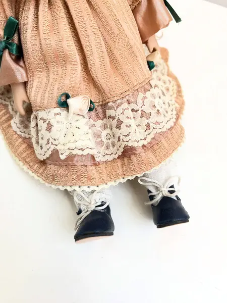 Foto de um(a) ​Boneca de porcelana, da categoria de Brinquedos e Hobbies. Boneca de porcelana com leves marcas do tempo e uso. Com suporte. Medidas: 30x16cm. Mostrado de uma perspectiva diferente. Vendido no marketplace Trésors.