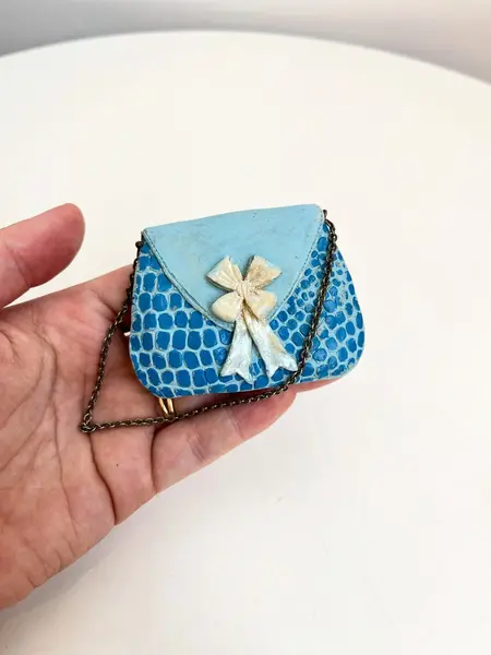 Foto de um(a) ​Bolsinha colecionável em resina, da categoria de Outros colecionáveis. Bolsinha colecionável em resina com alça em corrente metálica. Apresenta desgastes na pintura como nas fotos. Medidas: 6x8cm. Mostrado de uma perspectiva diferente. Vendido no marketplace Trésors.