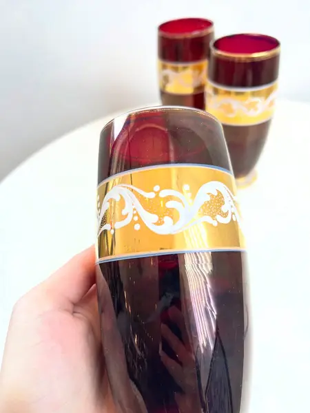Foto de um(a) ​Trio de copos altos de vidro da década de 50, da categoria de Copos. Trio de copos altos de vidro da década de 50, pintados em bordô, dourado e branco. Marcas do tempo e uso e um com mínimo... Mostrado de uma perspectiva diferente. Vendido no marketplace Trésors.