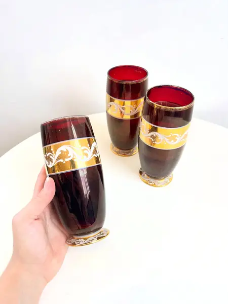 Foto de um(a) ​Trio de copos altos de vidro da década de 50, da categoria de Copos. Trio de copos altos de vidro da década de 50, pintados em bordô, dourado e branco. Marcas do tempo e uso e um com mínimo... Mostrado de uma perspectiva diferente. Vendido no marketplace Trésors.
