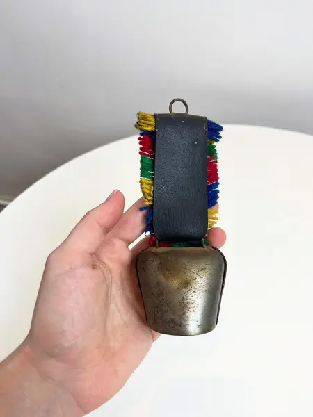 Foto de um(a) Sino suiço em metal, da categoria de Memorabilia de viagem & souvenir. Sino suíço em metal estampado, couro e lã. Marcas do tempo e uso como nas fotos. Medidas: 16x6cm. Mostrado de uma perspectiva diferente. Vendido no marketplace Trésors.