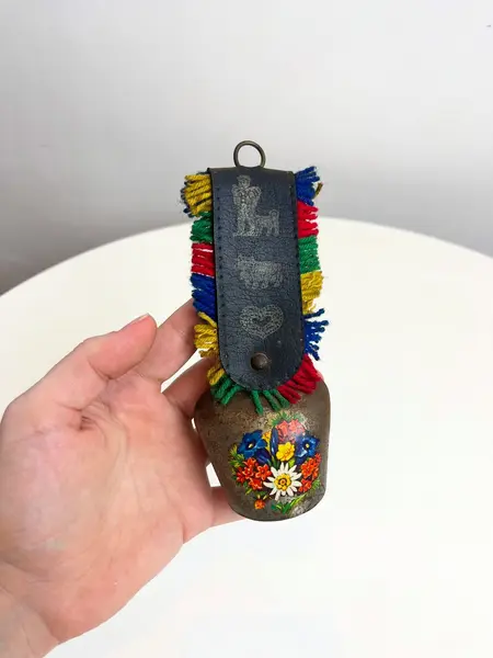Foto de um(a) Sino suiço em metal, da categoria de Memorabilia de viagem & souvenir. Sino suíço em metal estampado, couro e lã. Marcas do tempo e uso como nas fotos. Medidas: 16x6cm. Mostrado de uma perspectiva diferente. Vendido no marketplace Trésors.