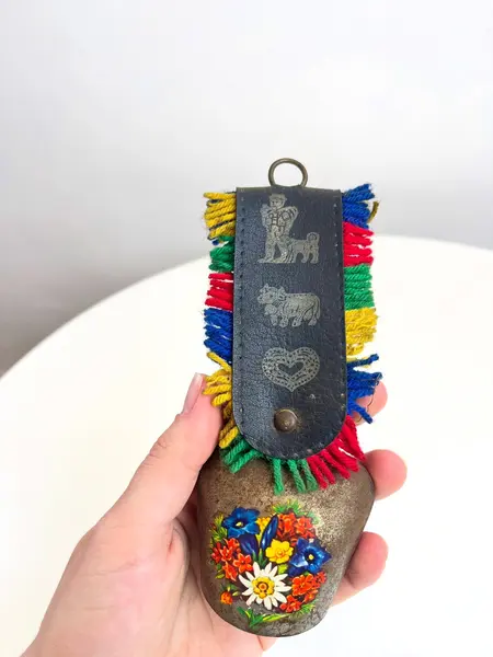 Foto de um(a) Sino suiço em metal, da categoria de Memorabilia de viagem & souvenir. Sino suíço em metal estampado, couro e lã. Marcas do tempo e uso como nas fotos. Medidas: 16x6cm. Mostrado de uma perspectiva diferente. Vendido no marketplace Trésors.