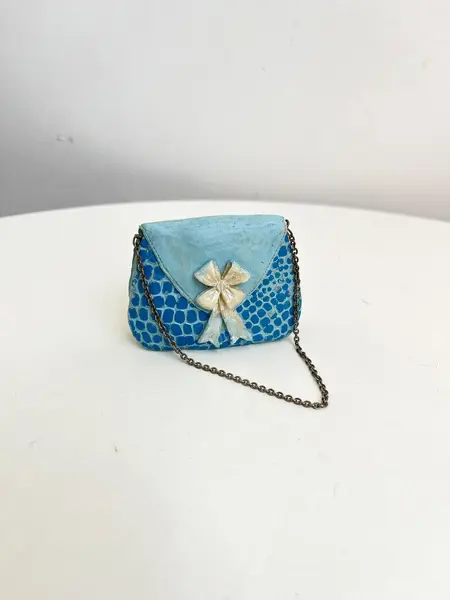 Foto de um(a) ​Bolsinha colecionável em resina, da categoria de Outros colecionáveis. Bolsinha colecionável em resina com alça em corrente metálica. Apresenta desgastes na pintura como nas fotos. Medidas: 6x8cm. Mostrado de uma perspectiva diferente. Vendido no marketplace Trésors.