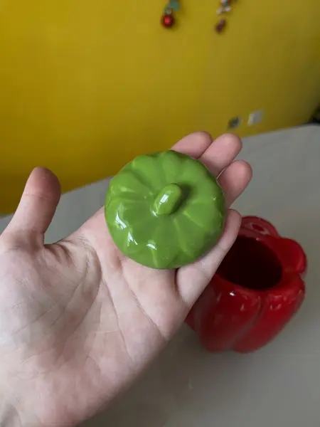 Foto de um(a) ​Pote com tampa em cerâmica formato pimentão, da categoria de Garrafas, potes e jarros. Pote com tampa em cerâmica. Possui lascado interno na tampa como mostrado nas fotos. Medidas: 12x10cm. Mostrado de uma perspectiva diferente. Vendido no marketplace Trésors.