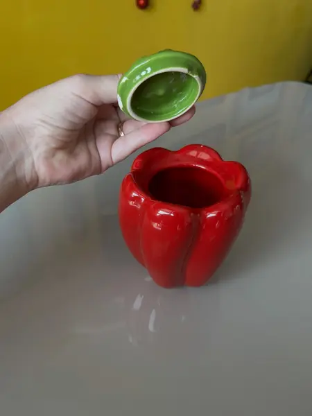 Foto de um(a) ​Pote com tampa em cerâmica formato pimentão, da categoria de Garrafas, potes e jarros. Pote com tampa em cerâmica. Possui lascado interno na tampa como mostrado nas fotos. Medidas: 12x10cm. Mostrado de uma perspectiva diferente. Vendido no marketplace Trésors.