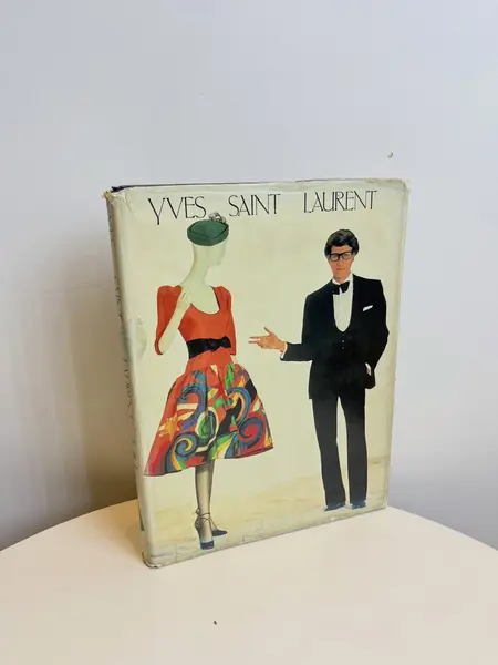 Foto de um(a) Livro capa dura Yves Saint Laurent 1983, da categoria de Livros. Maravilhoso livro capa dura em tecido, em inglês, de 1983. Marcas do tempo e uso. Mostrado de uma perspectiva diferente. Vendido no marketplace Trésors.