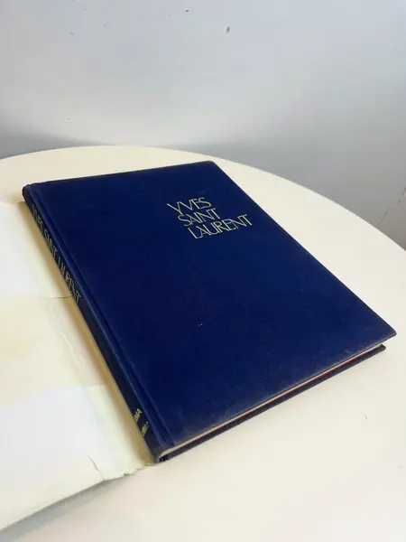 Foto de um(a) Livro capa dura Yves Saint Laurent 1983, da categoria de Livros. Maravilhoso livro capa dura em tecido, em inglês, de 1983. Marcas do tempo e uso. Mostrado de uma perspectiva diferente. Vendido no marketplace Trésors.