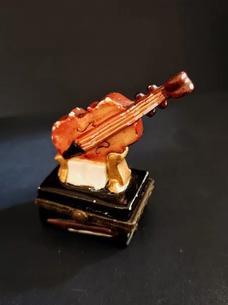 Foto de um(a) Caixinha de Porcelana Violino, Década de 2000, da categoria de Cestos e Caixas. Caixa em porcelana policromada com fecho em latão oxidado, década de 2000.A: 7,3 cm L: 4,8 cm P: 3,3 cm peso: 70g. Mostrado de uma perspectiva diferente. Vendido no marketplace Trésors.