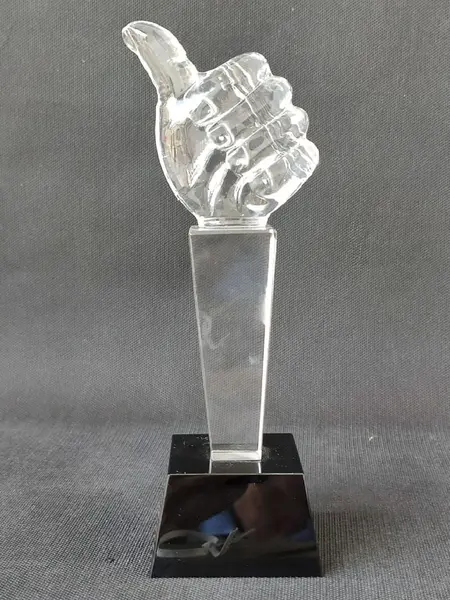Foto de um(a) Troféu Joinha Cristal, da categoria de Escultura. Escultura em cristal do joinha, base um prisma de quatro faces em cristal preto.A: 21cm Base: 6.5 x 7 x 4.5 cm Peso: 718g. Mostrado de uma perspectiva diferente. Vendido no marketplace Trésors.