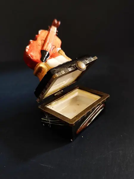 Foto de um(a) Caixinha de Porcelana Violino, Década de 2000, da categoria de Cestos e Caixas. Caixa em porcelana policromada com fecho em latão oxidado, década de 2000.A: 7,3 cm L: 4,8 cm P: 3,3 cm peso: 70g. Mostrado de uma perspectiva diferente. Vendido no marketplace Trésors.