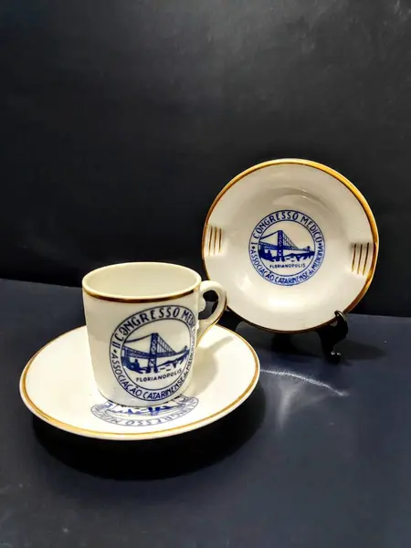 Foto de um(a) Conjunto Cafézinho e Cinzeiro, II Congresso Médico em Florianópolis, Porcelana Schmidt, Anos 2000, da categoria de Xícaras. Xícara de cafézinho e cinzeiro com logo do II congresso médico em florianópolis: porcelana schmidt com filete em ouro e logo... Mostrado de uma perspectiva diferente. Vendido no marketplace Trésors.