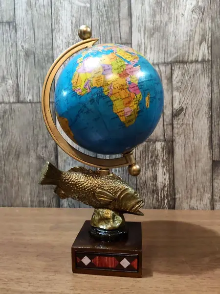 Foto de um(a) Globo Terrestre Latão e Marchetaria anos 70, da categoria de Globos. Globo terrestre de mesa com globo giratório e envelhecido com base de peixe em latão e madeira com marchetaria adesivada... Mostrado de uma perspectiva diferente. Vendido no marketplace Trésors.