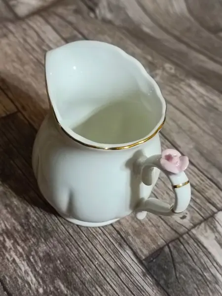 Foto de um(a) Cremeira Porcelana Branca Wolff, Década de 2010, da categoria de Cremeiras. Cremeira em porcelana branca lisa levemente canelada, com filete em ouro na borda e alça e detalhe de rosa na cor rosa,... Mostrado de uma perspectiva diferente. Vendido no marketplace Trésors.