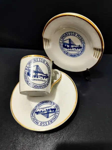 Foto de um(a) Conjunto Cafézinho e Cinzeiro, II Congresso Médico em Florianópolis, Porcelana Schmidt, Anos 2000, da categoria de Xícaras. Xícara de cafézinho e cinzeiro com logo do II congresso médico em florianópolis: porcelana schmidt com filete em ouro e logo... Mostrado de uma perspectiva diferente. Vendido no marketplace Trésors.