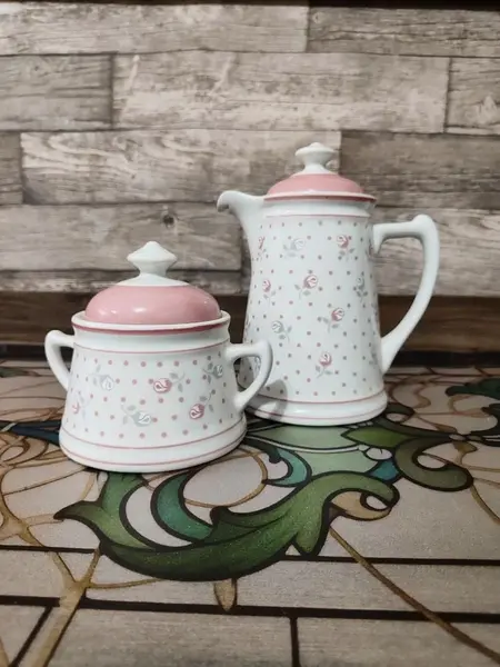 Foto de um(a) Bule e Açucareiro Porcelana Real, Década de 1990, da categoria de Bules. Combo com bule e açucareiro em porcelana branca e estampa de flores em rosa e cinza. Bule com trava na tampa e tranca pingo.... Mostrado de uma perspectiva diferente. Vendido no marketplace Trésors.