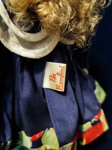 Foto de um(a) Boneca Porcelana e Tecido, Per Bambino, Década de 1990, da categoria de Bonecas. Boneca com membros e cabeça em porcelana, corpo em tecido/enchimento. Vestido original, cabelos de vinil e acompanha suporte... Mostrado de uma perspectiva diferente. Vendido no marketplace Trésors.