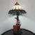 Foto de um(a) Abajur estilo Tiffany com escultura de palhaço, da categoria de Abajures. Bellisimo abajur estilo Tiffany com escultura de palhaço lendo livro. Medidas: altura 48 cm x diâmetro cúpula 28 cm x base... Mostrado de uma perspectiva diferente. Vendido no marketplace Trésors.