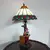 Foto de um(a) Abajur estilo Tiffany com escultura de palhaço, da categoria de Abajures. Bellisimo abajur estilo Tiffany com escultura de palhaço lendo livro. Medidas: altura 48 cm x diâmetro cúpula 28 cm x base... Mostrado de uma perspectiva diferente. Vendido no marketplace Trésors.