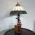 Foto de um(a) Abajur estilo Tiffany com escultura de palhaço, da categoria de Abajures. Bellisimo abajur estilo Tiffany com escultura de palhaço lendo livro. Medidas: altura 48 cm x diâmetro cúpula 28 cm x base... Mostrado de uma perspectiva diferente. Vendido no marketplace Trésors.