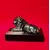 Foto de um(a) Troféu Leão do Ano, 71/72, da categoria de Escultura. Troféu Lions 1971/1972 - Leão do Ano. Em bronze com base de granito preto. A: 7 cm / L: 12 cm / P: 7,4 cm peso: 738 g. Mostrado de uma perspectiva diferente. Vendido no marketplace Trésors.