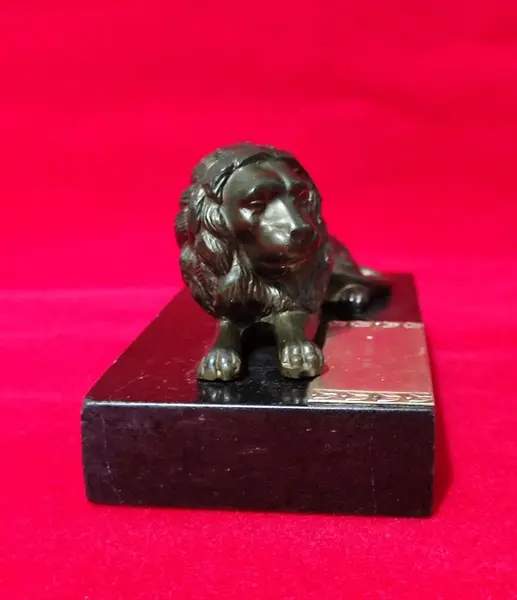 Foto de um(a) Troféu Leão do Ano, 71/72, da categoria de Escultura. Troféu Lions 1971/1972 - Leão do Ano. Em bronze com base de granito preto. A: 7 cm / L: 12 cm / P: 7,4 cm peso: 738 g. Mostrado de uma perspectiva diferente. Vendido no marketplace Trésors.