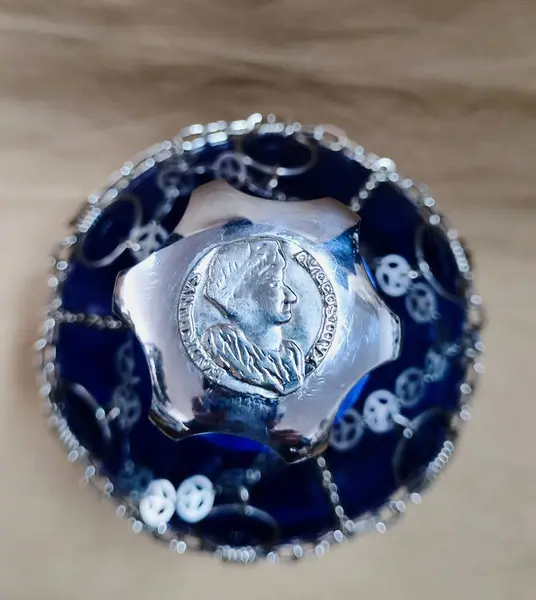 Foto de um(a) Garrafão com Malha Metálica, da categoria de Garrafas, potes e jarros. Garrafão em vidro azul com revestimento de malha metálica niquelada com correntes, aros e estampa de moeda romana e tampa... Mostrado de uma perspectiva diferente. Vendido no marketplace Trésors.
