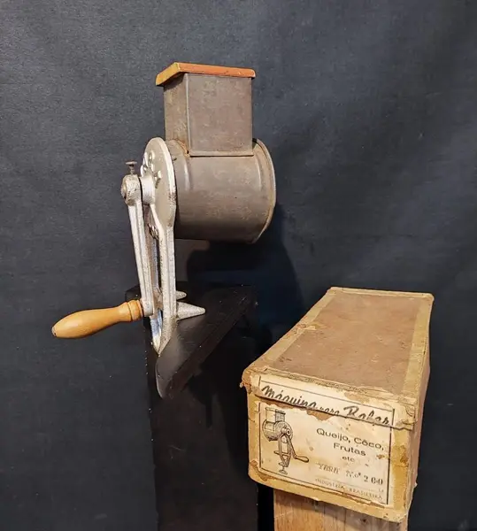 Foto de um(a) Ralador de Queijo e Frutas, Marca Yara N.200, Década de 1940, da categoria de Acessórios de cozinha. Máquina de ralar queijo, coco e frutas. Em ferro, folha de flanders e socador e manivela em madeira, com embalagem original... Mostrado de uma perspectiva diferente. Vendido no marketplace Trésors.