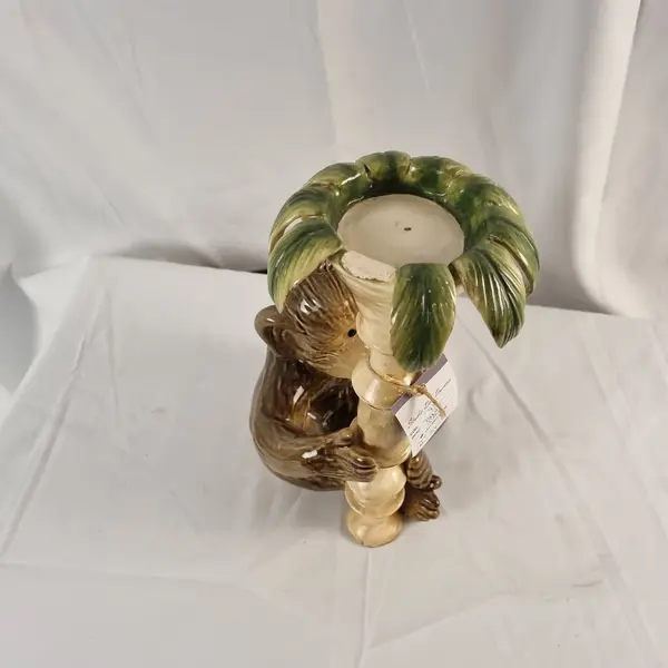 Foto de um(a) Castiçal em Cerâmica em Forma de Macaco, da categoria de Castiçais. Castiçal fabricado em cerâmica, representando um macaco junto a um pilar com folhas. Mostrado de uma perspectiva diferente. Vendido no marketplace Trésors.