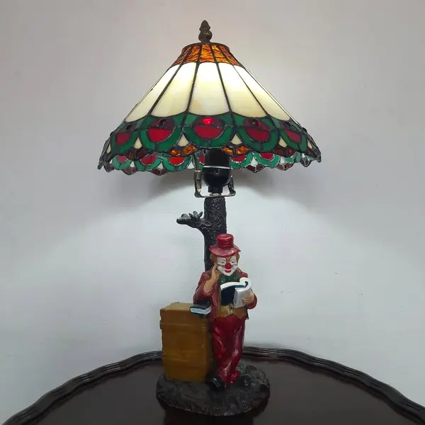 Foto de um(a) Abajur estilo Tiffany com escultura de palhaço, da categoria de Abajures. Bellisimo abajur estilo Tiffany com escultura de palhaço lendo livro. Medidas: altura 48 cm x diâmetro cúpula 28 cm x base... Mostrado de uma perspectiva diferente. Vendido no marketplace Trésors.