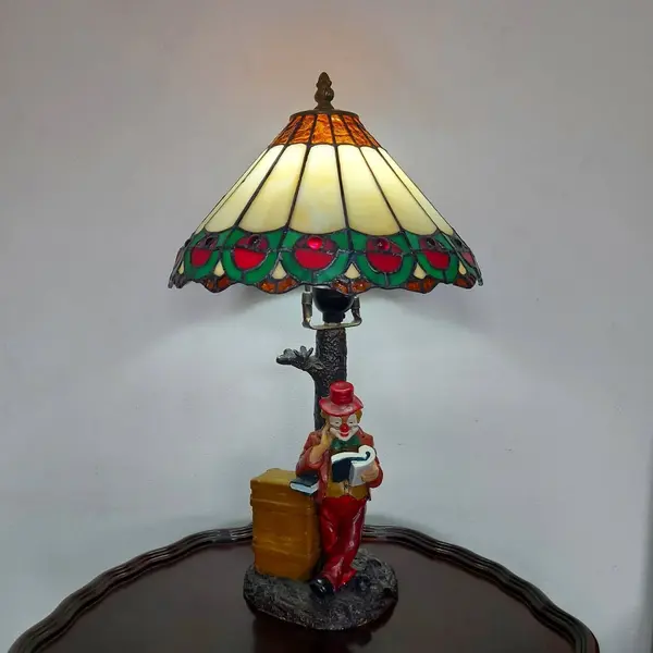 Foto de um(a) Abajur estilo Tiffany com escultura de palhaço, da categoria de Abajures. Bellisimo abajur estilo Tiffany com escultura de palhaço lendo livro. Medidas: altura 48 cm x diâmetro cúpula 28 cm x base... Mostrado de uma perspectiva diferente. Vendido no marketplace Trésors.
