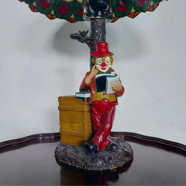Foto de um(a) Abajur estilo Tiffany com escultura de palhaço, da categoria de Abajures. Bellisimo abajur estilo Tiffany com escultura de palhaço lendo livro. Medidas: altura 48 cm x diâmetro cúpula 28 cm x base... Mostrado de uma perspectiva diferente. Vendido no marketplace Trésors.