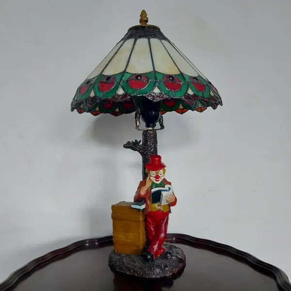 Foto de um(a) Abajur estilo Tiffany com escultura de palhaço, da categoria de Abajures. Bellisimo abajur estilo Tiffany com escultura de palhaço lendo livro. Medidas: altura 48 cm x diâmetro cúpula 28 cm x base... Mostrado de uma perspectiva diferente. Vendido no marketplace Trésors.