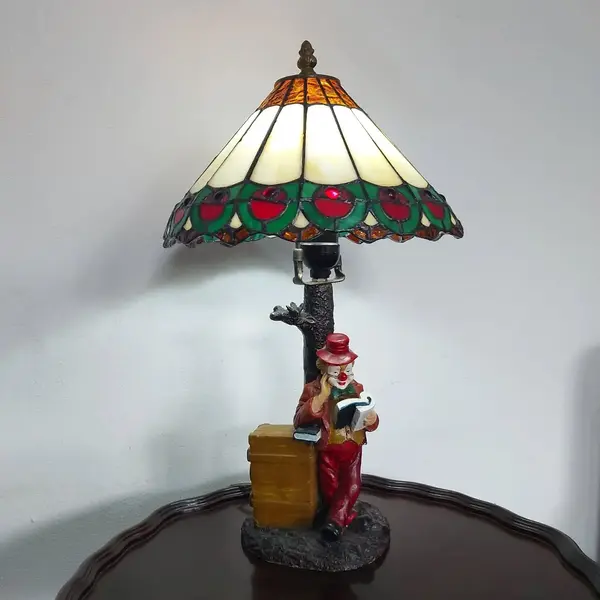 Foto de um(a) Abajur estilo Tiffany com escultura de palhaço, da categoria de Abajures. Bellisimo abajur estilo Tiffany com escultura de palhaço lendo livro. Medidas: altura 48 cm x diâmetro cúpula 28 cm x base... Mostrado de uma perspectiva diferente. Vendido no marketplace Trésors.