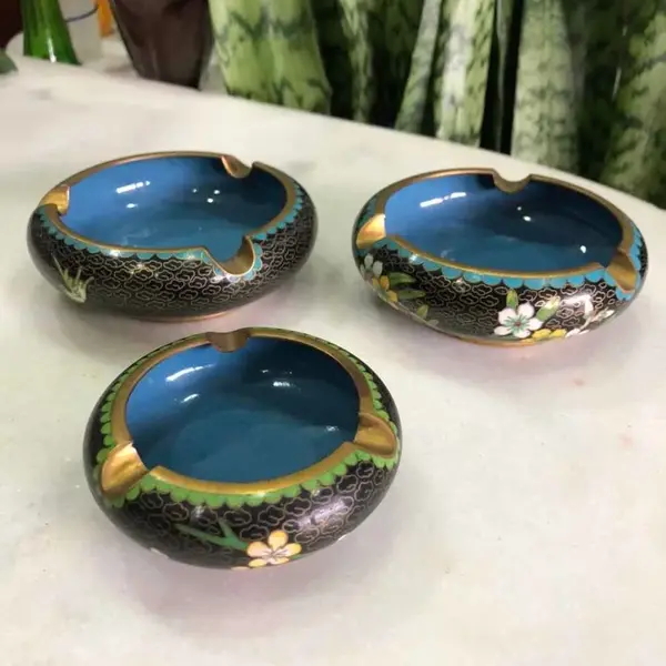 Foto de um(a) Antigo Trio De Cinzeiros Orientais Em Bronze Cloisonné, da categoria de Cinzeiros. Antigos e lindos cinzeiros orientais feitos à mão em Cloisonné. Decorados com flores e folhagens, com esmalte azul na parte... Mostrado de uma perspectiva diferente. Vendido no marketplace Trésors.