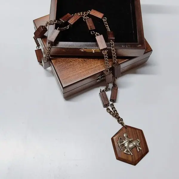 Foto de um(a) Colar em Jacarandá com Medalhão Signo de Sagitário, Década de 1970, da categoria de Outros colecionáveis. Colar de madeira de jacarandá dos anos 1970: corrente com 14 retângulos com base quadrada, unidos por corrente dourada... Mostrado de uma perspectiva diferente. Vendido no marketplace Trésors.
