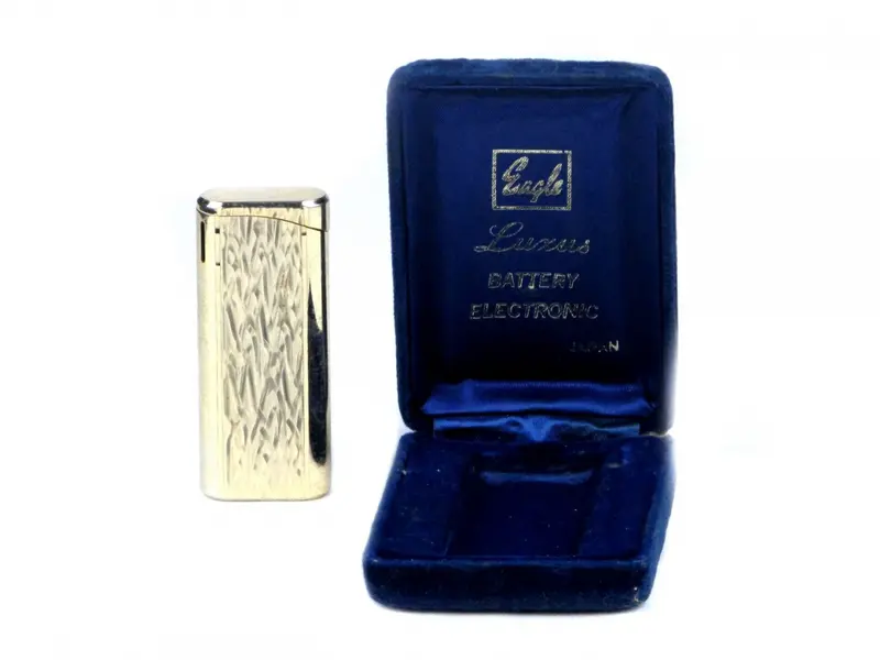 Foto de um(a) Antigo isqueiro EAGLE/ LUXUS, da categoria de Isqueiros e isqueiros. Antigo isqueiro em metal dourado da manufatura EAGLE/ LUXUS BATTERY ELECTRONIC JAPAN.No estojo original em veludo azul.... Vendido no marketplace Trésors.