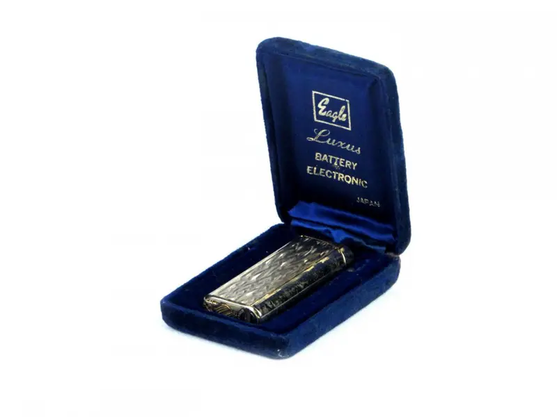 Foto de um(a) Antigo isqueiro EAGLE/ LUXUS, da categoria de Isqueiros e isqueiros. Antigo isqueiro em metal dourado da manufatura EAGLE/ LUXUS BATTERY ELECTRONIC JAPAN.No estojo original em veludo azul.... Mostrado de uma perspectiva diferente. Vendido no marketplace Trésors.